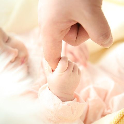 A baby, reaching out and holding a person's finger